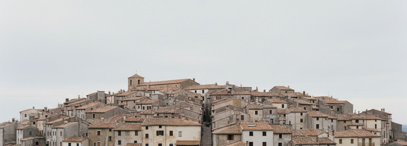 A small hill town photographed from a low ridge, the whole built area visible from one edge to the other under flat cloud.