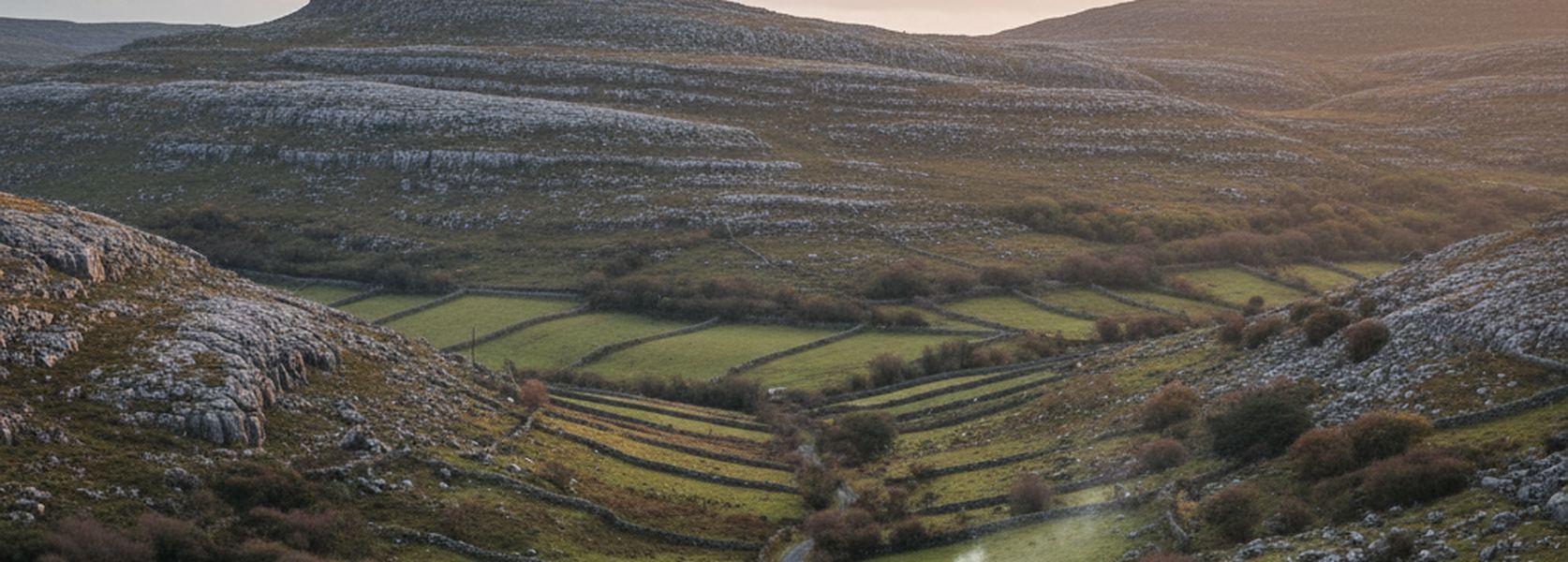 Terraced gray limestone hills above a narrow green valley in County Clare, small irregular fields divided by dry stone walls.