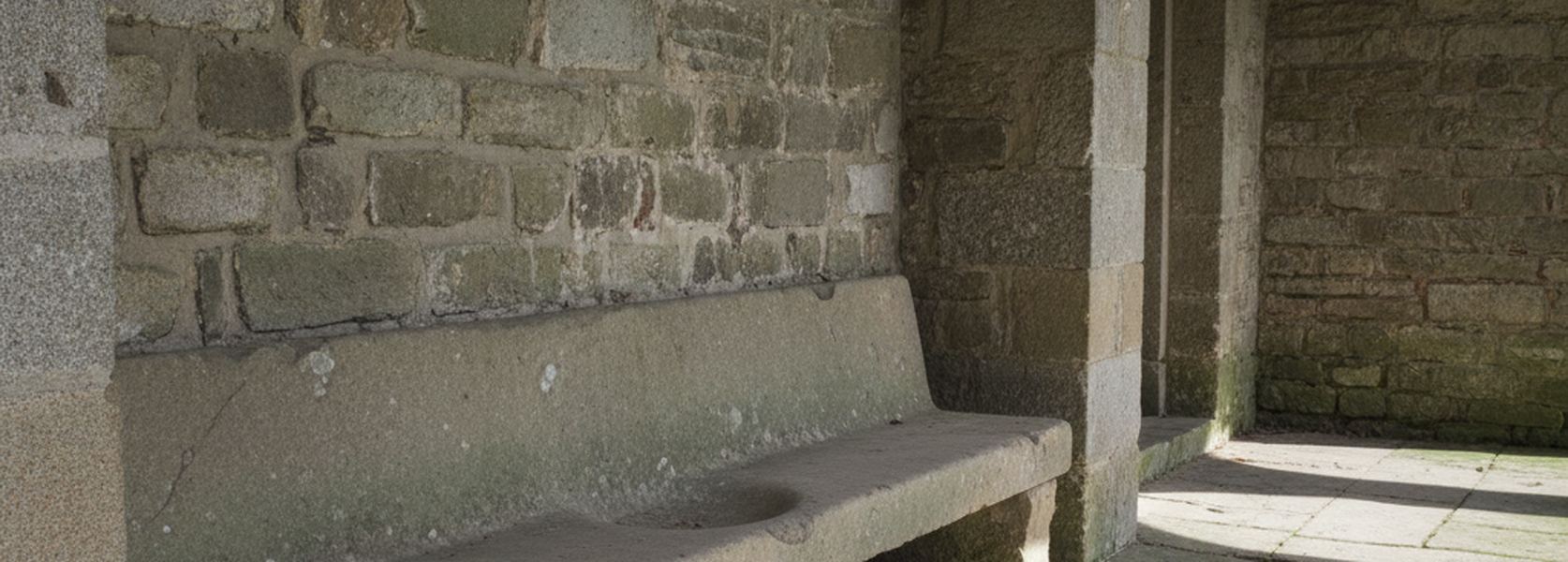 A long stone bench built into the wall of a shaded loggia, its seat slab worn smooth above large flagstones.